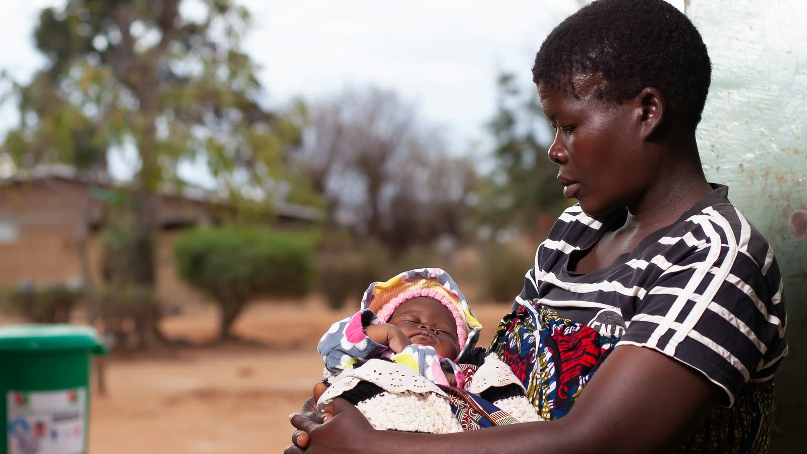 A mother holding her newborn baby outside a rural clinic
